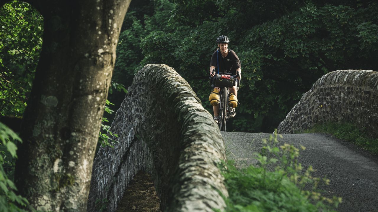 A cyclist rides over a small stone road bridge