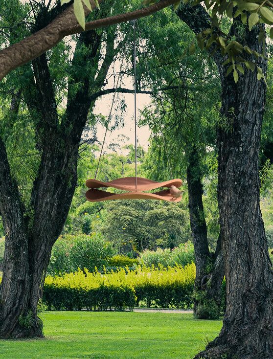 A ceramic, terracotta-shaded birdhouse sculpted from two identic, wavy surfaces resembling a spaceship hangs in between two trees from a tree branch.