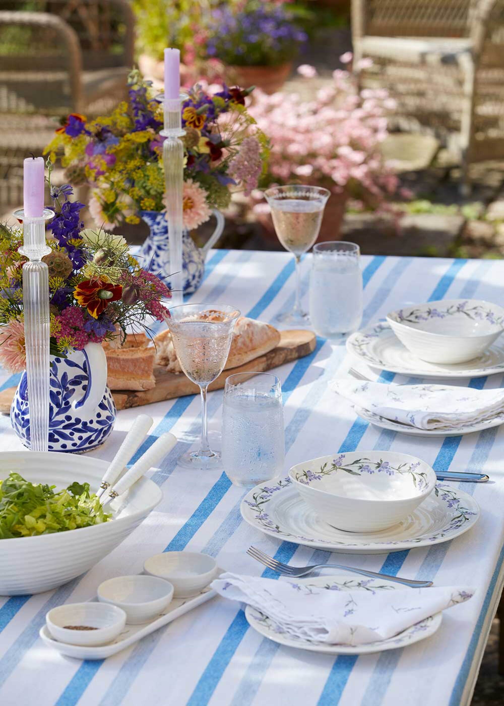 A table laid for dinner with china side plates, tall candles, and vases of flowers