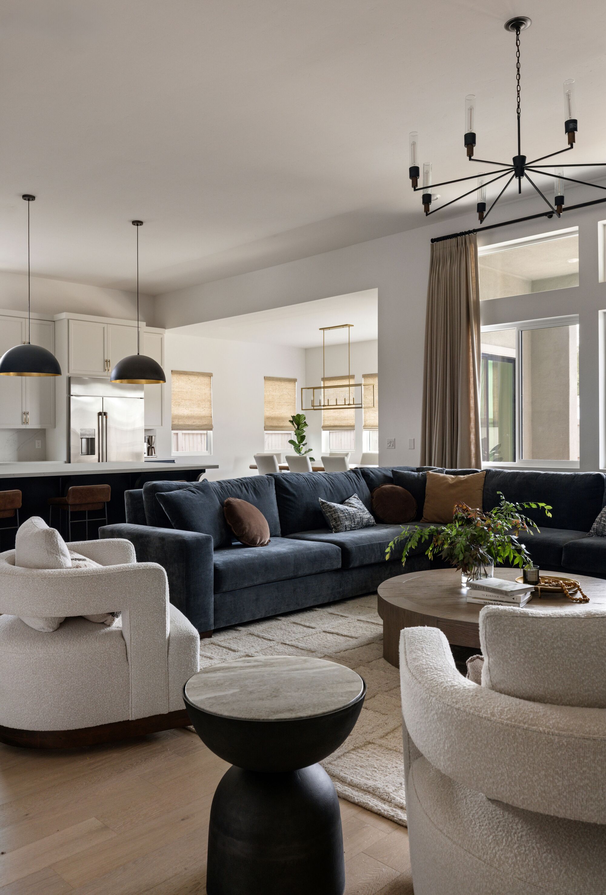 A living room with a large blue L-shaped sofa and two white curved boucle accent chairs