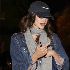 Kaia Gerber wears a baseball cap, gray scarf, and denim jacket.