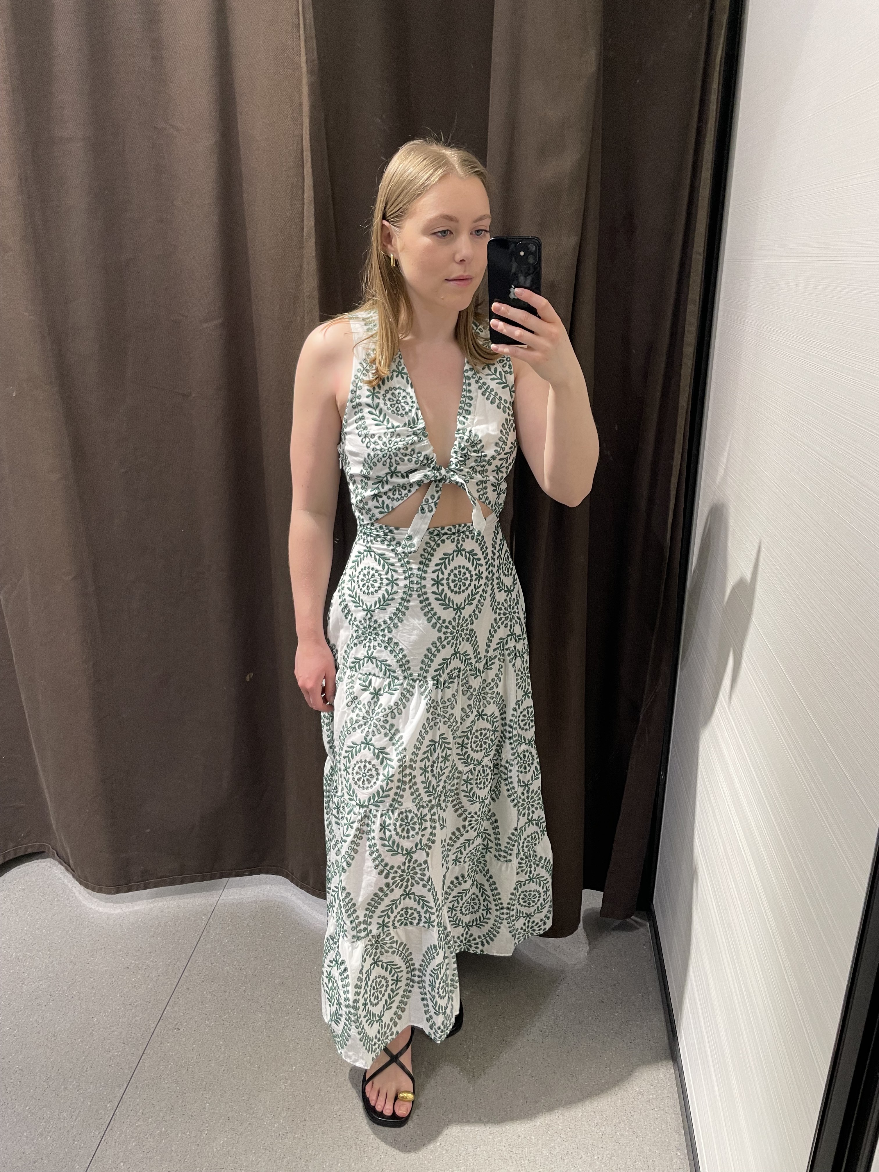 Woman in dressing room wears white dress with green embroidery