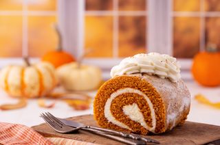 A pumpkin roll on a cutting board surrounded by baby pumpkins.