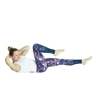 Woman in exercise clothes lies on her back, raising her legs with one parallel to the floor and bending the other knee, her hands behind her raised head, looking to the side, doing criss-cross exercise