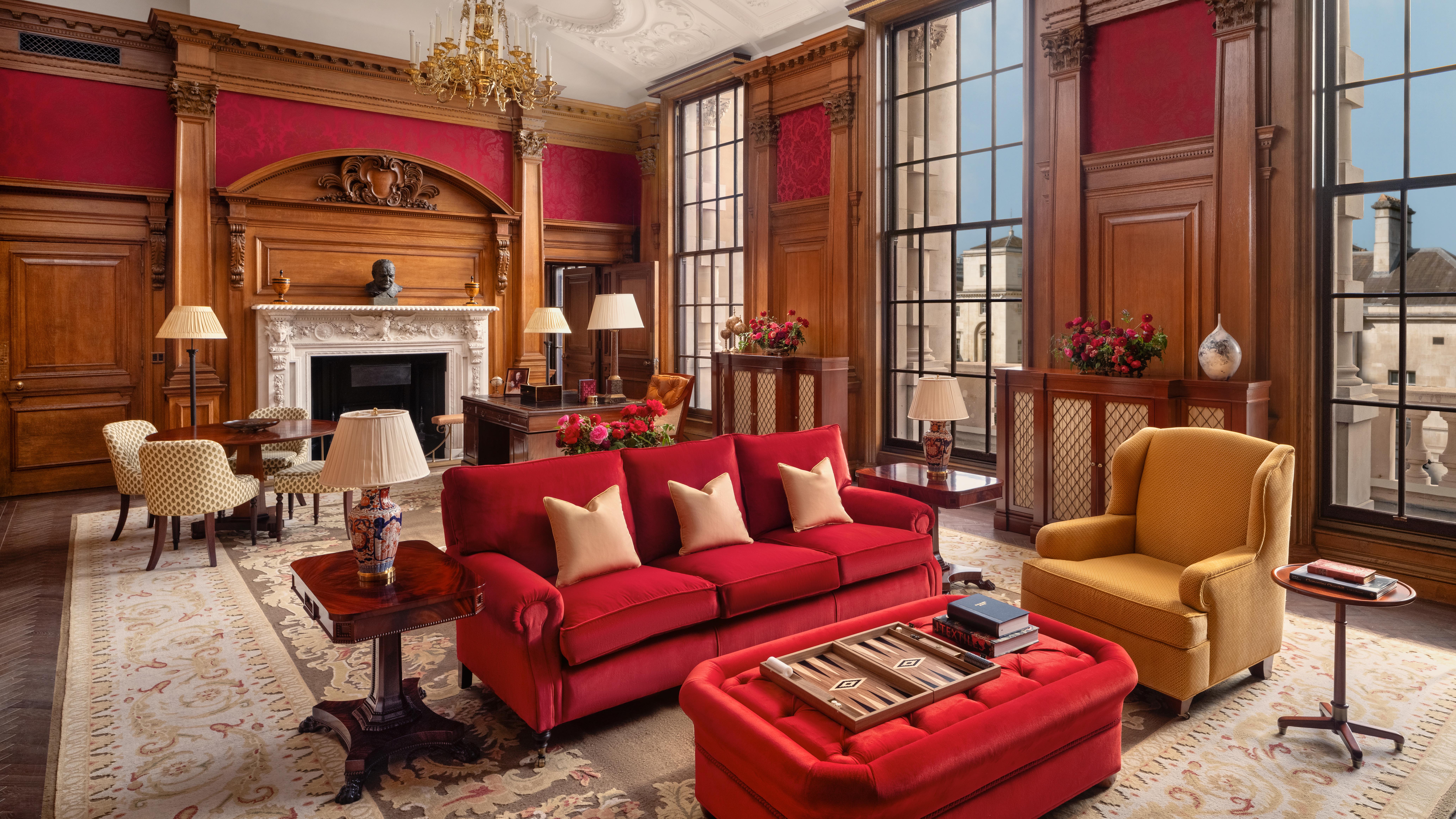 Red fabric wallpaper and wood panelled room with floor to ceiling windows overlooking Whitehall, red sofas and a yellow armchair