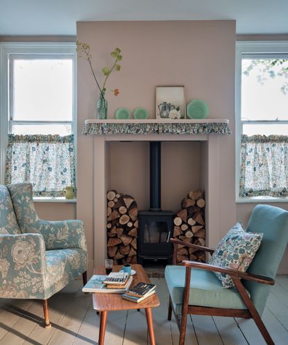 Pink living room with wooden floor, fireplace with logs and log burner, blue wooden armchair and blue plates on mantel