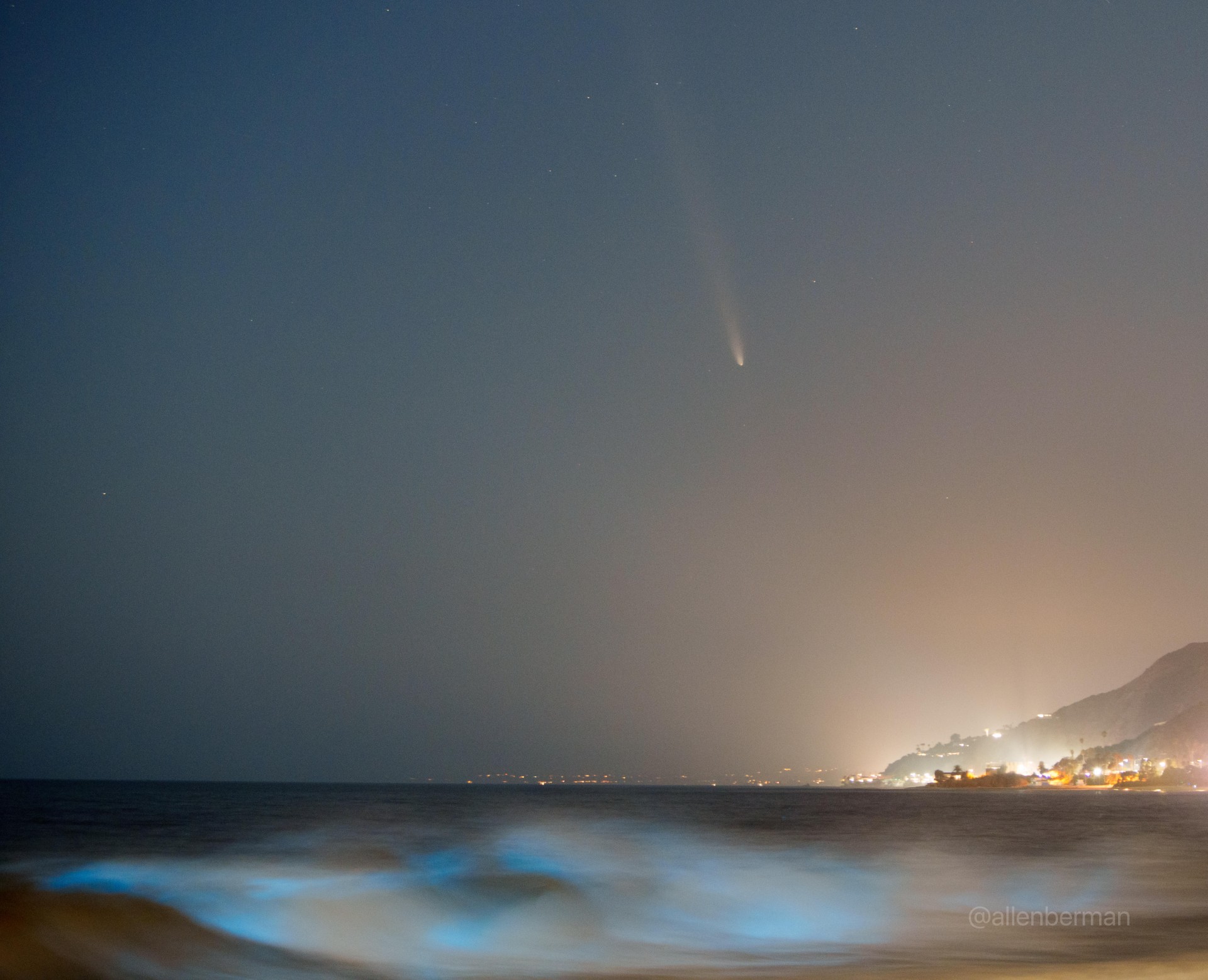 a fuzzy streak in the night sky above an ocean glowing pale blue