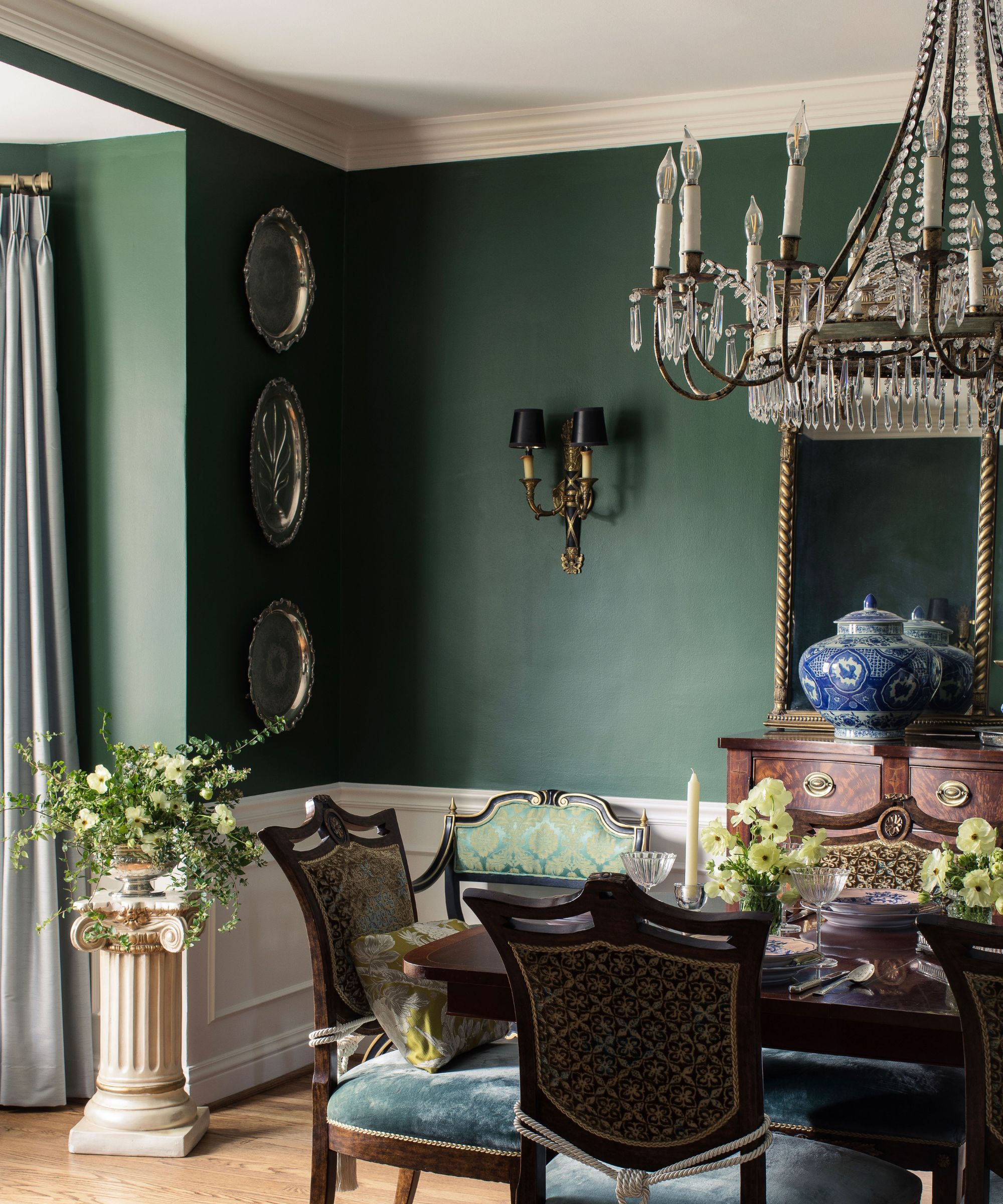 A green dining room with a large chandelier over the table and vintage sconces on the walls