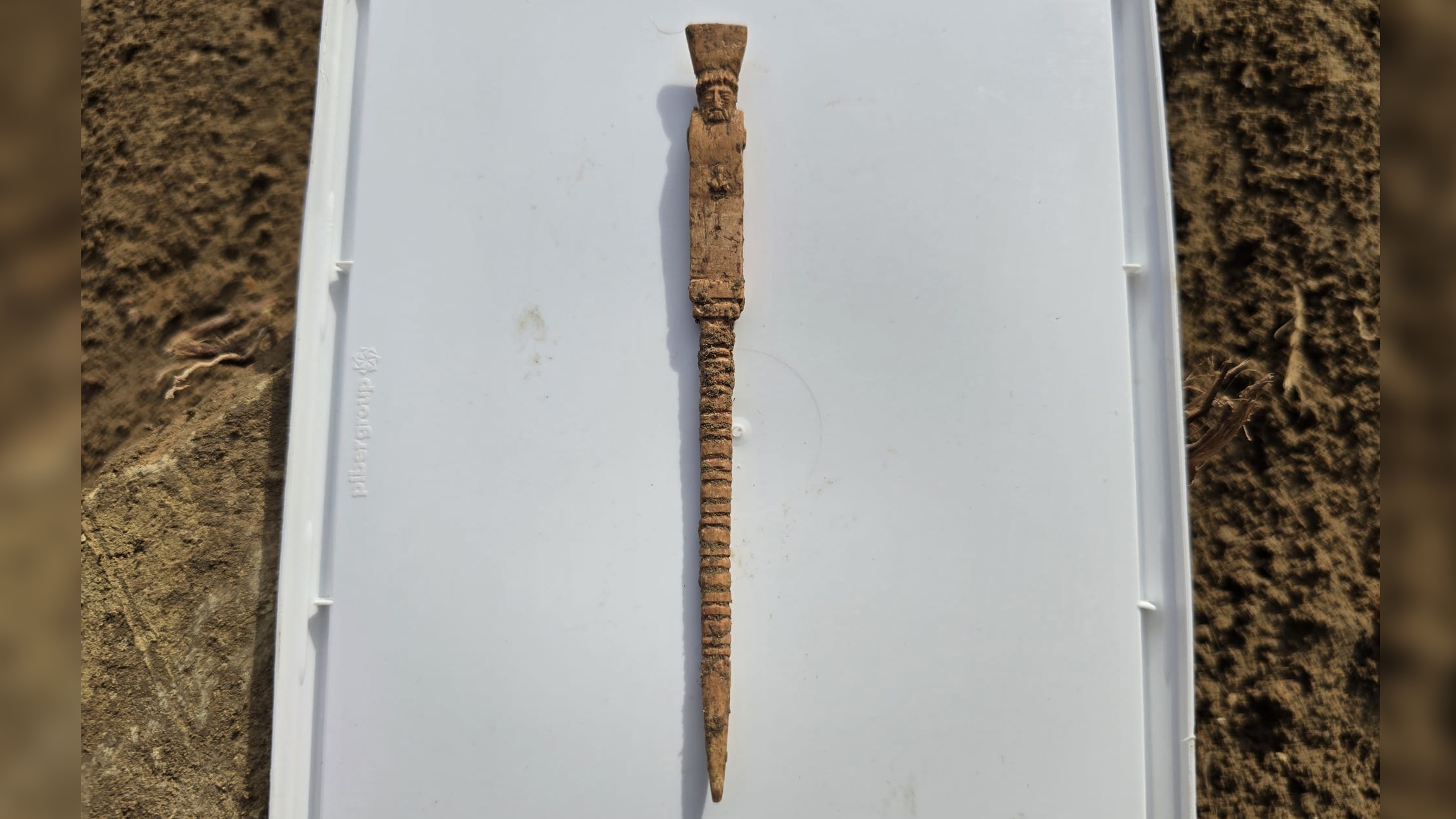a dirt-covered bone tool shaped like a grumpy man with a phallus
