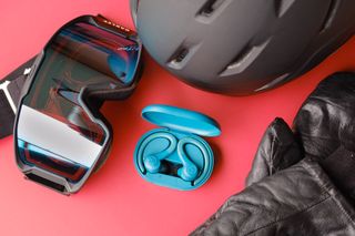 JLab Go Air Sport earbuds next to snowboard gear on red table.