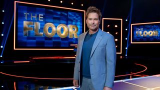 Rob Lowe, host of new Fox gameshow "The Floor", stands in a glitzy TV studio in front of screens displaying The Floor logo. 