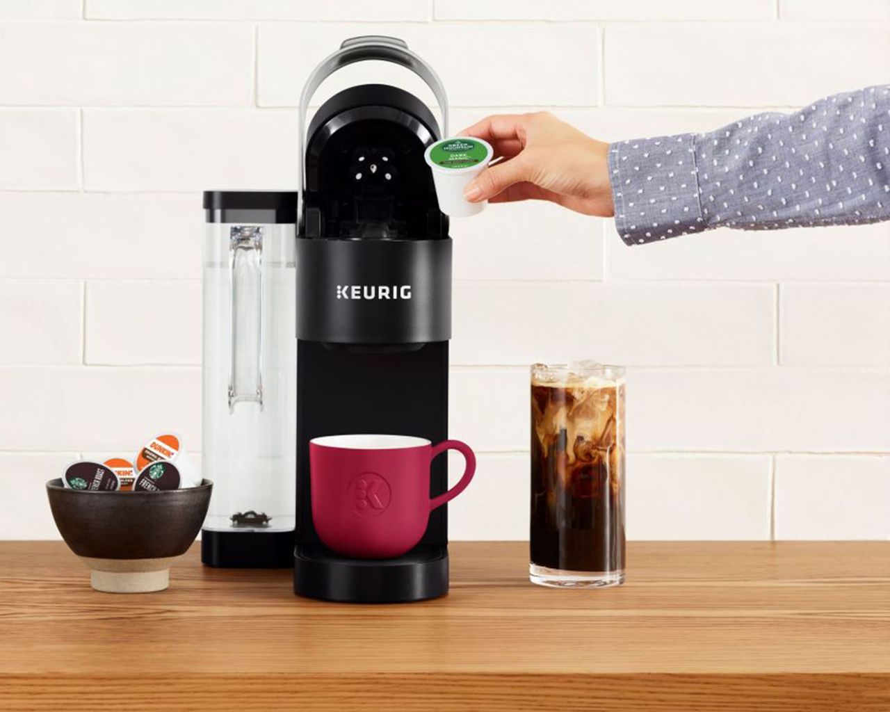 A female with light denim pattered blouse inserting K-Cup Keurig coffee capsule into coffee maker