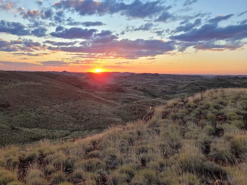 a photo of a sunset over dry, grassy rolling hills
