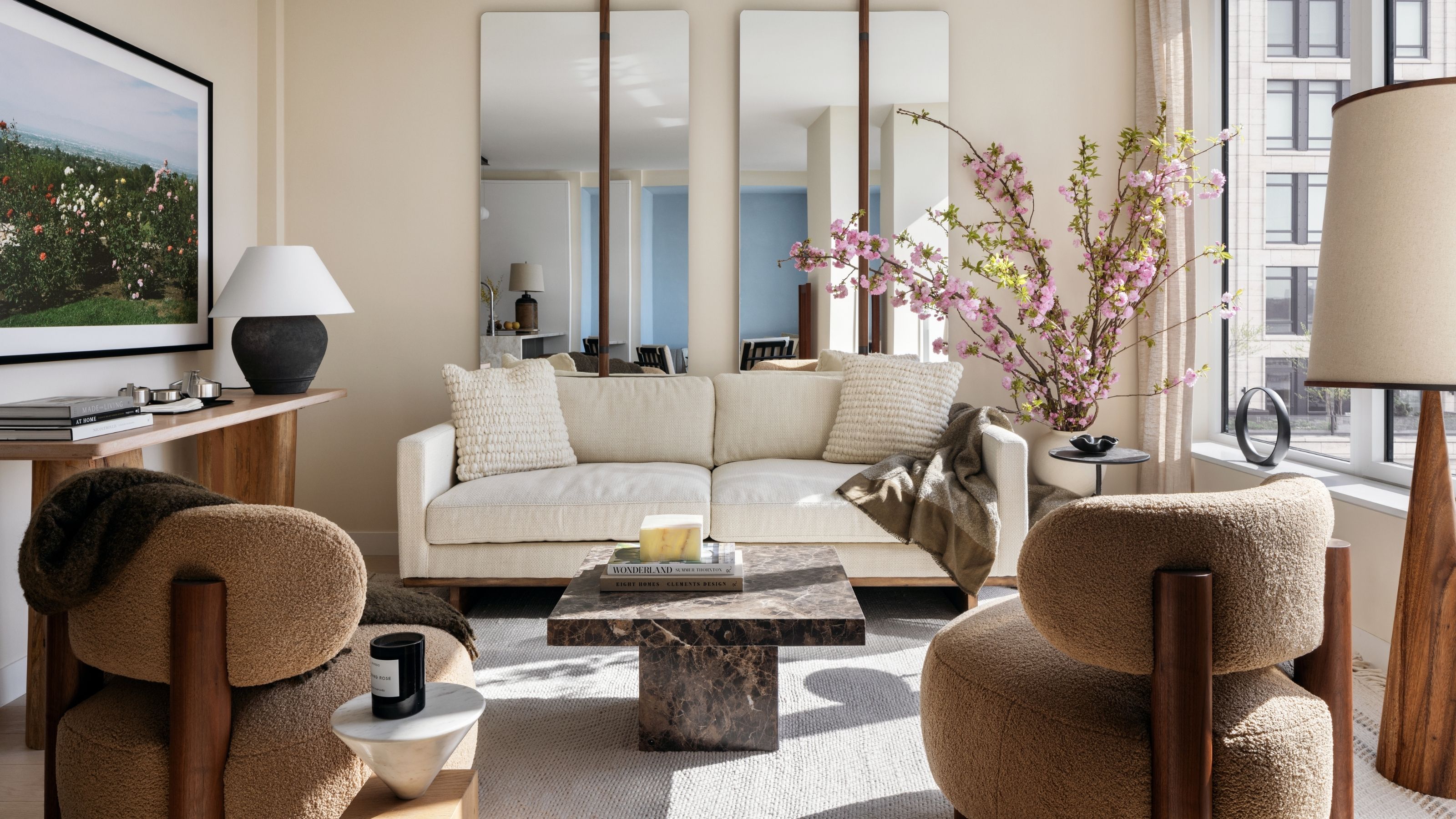 A small but elevated living room with lots of natural light. There is a white sofa, a dark marble coffee table, and two teddy brown armless accent chairs.