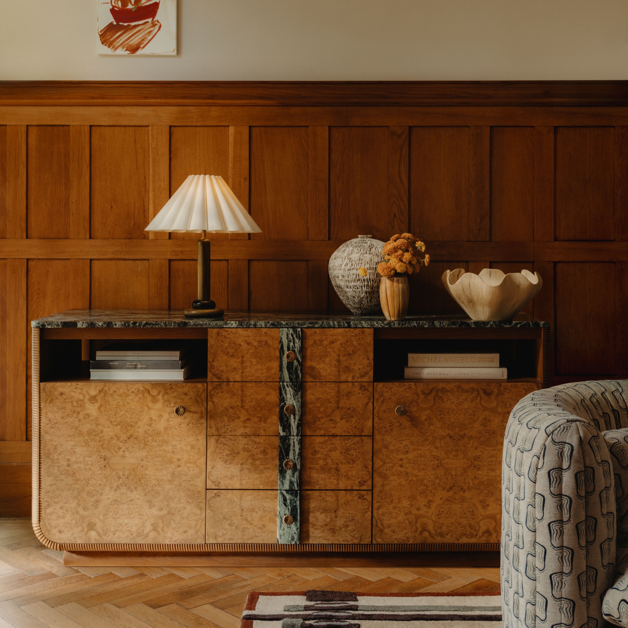A living room with wooden wall panelling and a burl wood and stone sideboard from Soho Home