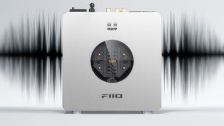Product shot of the FiiO K13 R2R DAC on a light grey background with a black sound wave image behind it