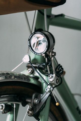 A silver lamp on the fork of a green classic bike