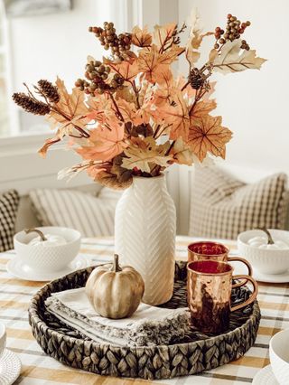 Dried orange flowers in a neutral vase on a wicker tray with orange mugs