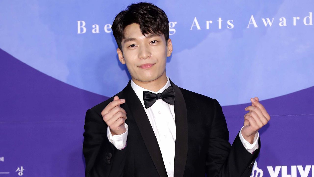 south korean Wi Ha-joon poses in a tux with his hands making hearts on a red carpet