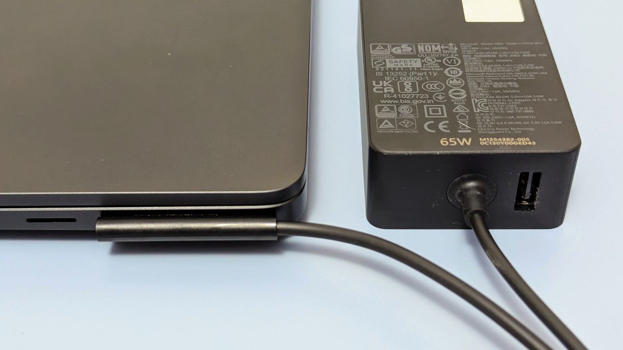 Close up of magnetic charging port and connector with power brick beside the Microsoft Surface Laptop 7