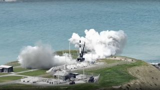 a black and white rocket stands on a seaside launch pad with smoke billowing around its base