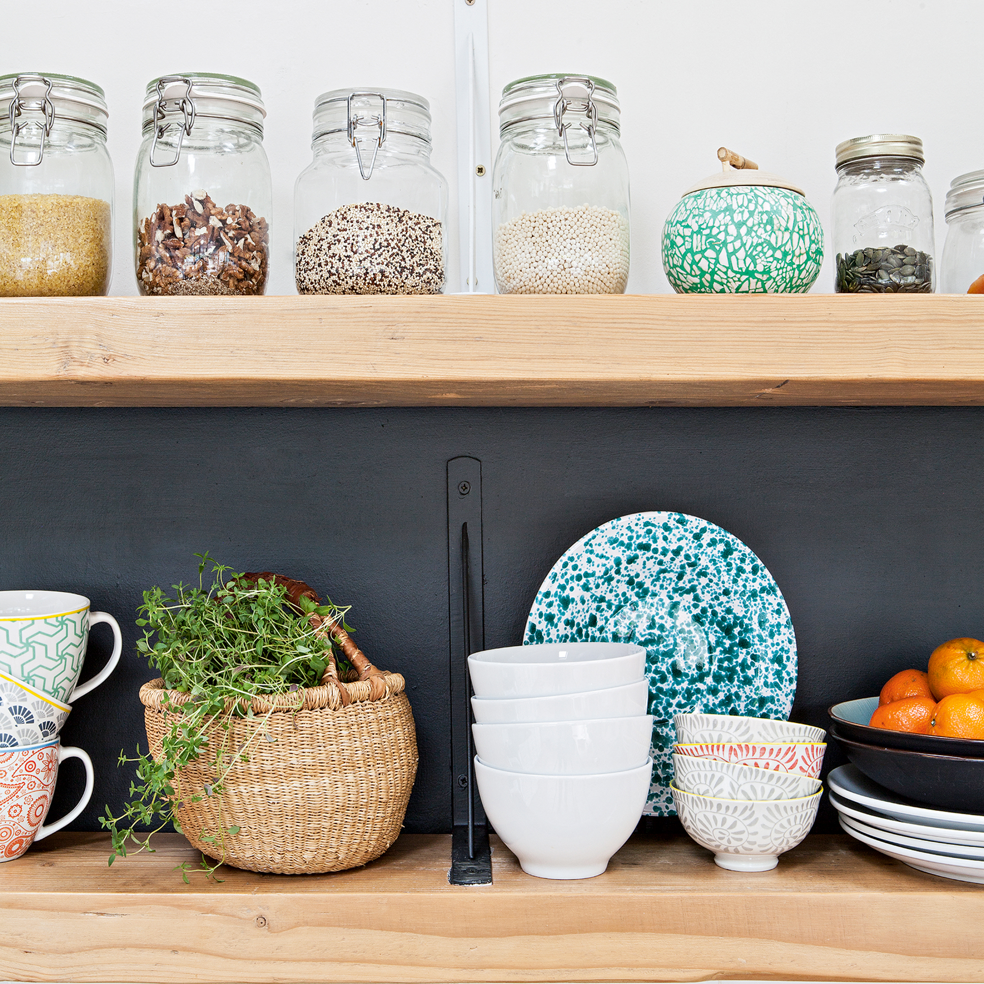 Open kitchen shelving with jars of grains and collection of mugs, bowls and plates
