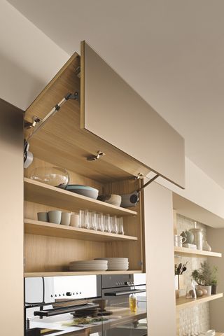 Hinged kitchen cabinet with door opening vertically filled with tableware