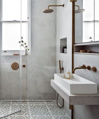 A bathroom with a walk in shower, neutral walls, tiled floors and copper fittings