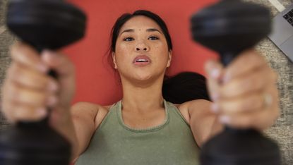 Woman lying on an exercise mat exercising with dumbbells