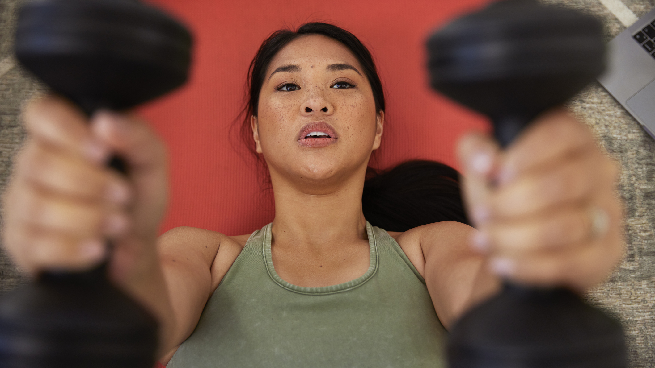 Woman lying on an exercise mat exercising with dumbbells