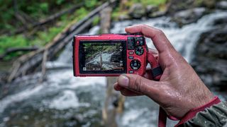Olympus Tough TG-6 review: hand holding Tough TG-6 camera with LCD screen displaying image of forest river