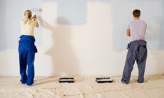 man and a woman couple painting a wall blue with rollers, and dust sheets on the floor