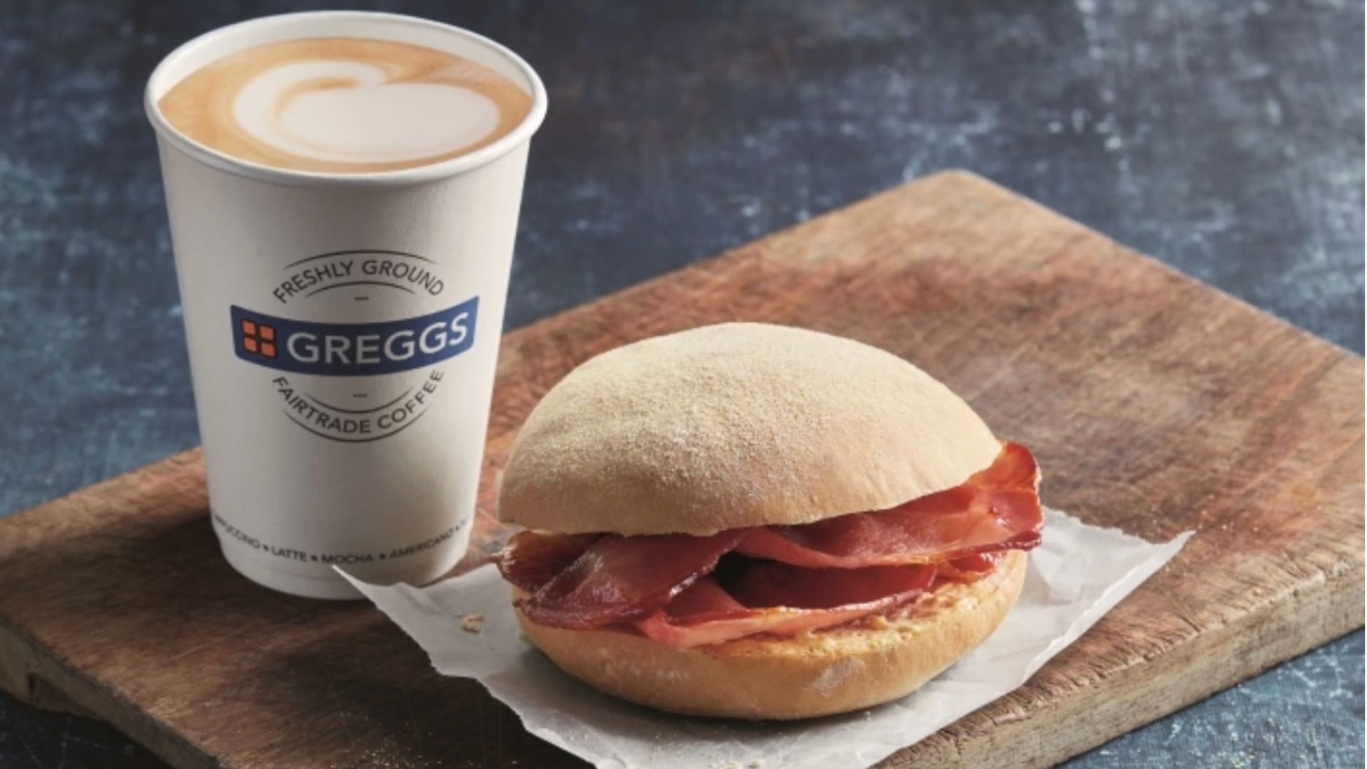 an image of a Greggs coffee and bacon bap on a wooden bord