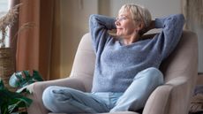 An older woman looks serene as she sits in an armchair and looks out the window.