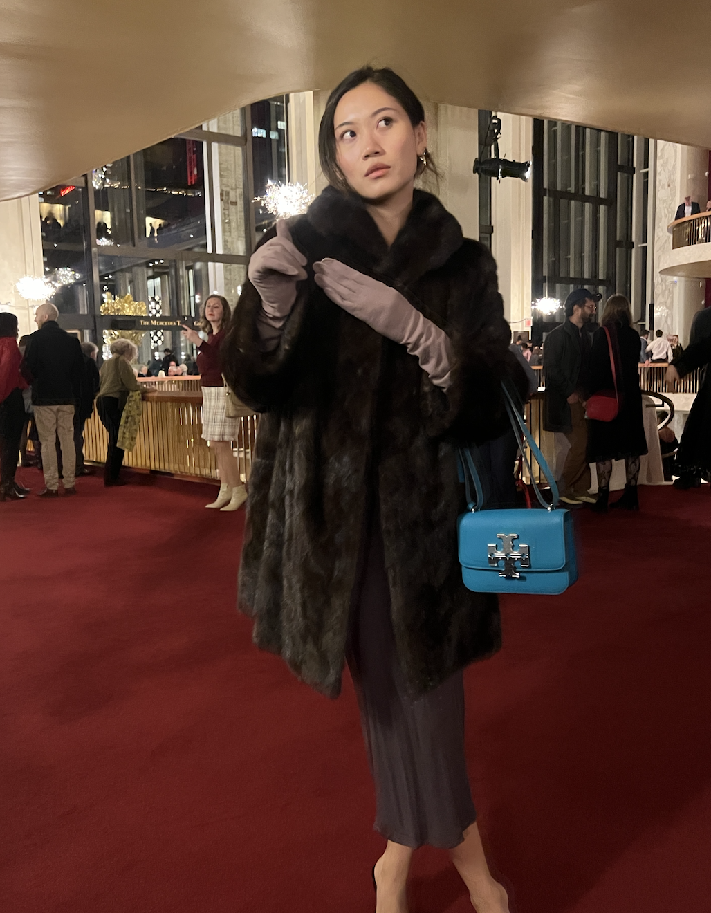 Vivian Li wearing a gray dress, brown fur jacket, purple gloves, and blue bag