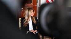 Melania Trump sitting in the Blue Room of the White House, a blurred camera lens in the foreground
