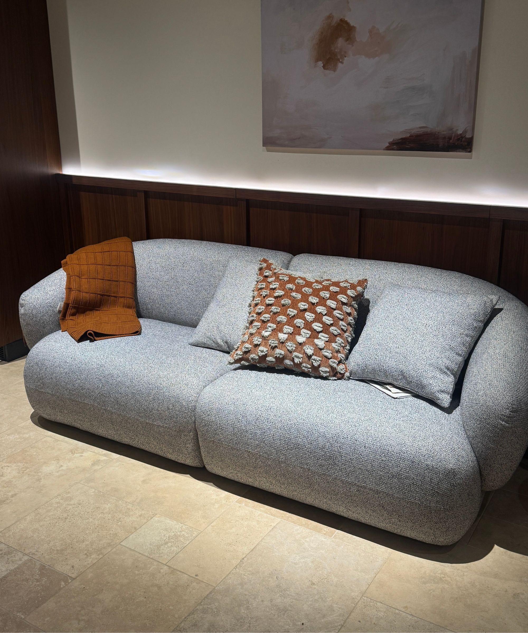 Castlery sofa with colorful, patterned cushions in front of timber panelling with artwork on wall and tiled floor