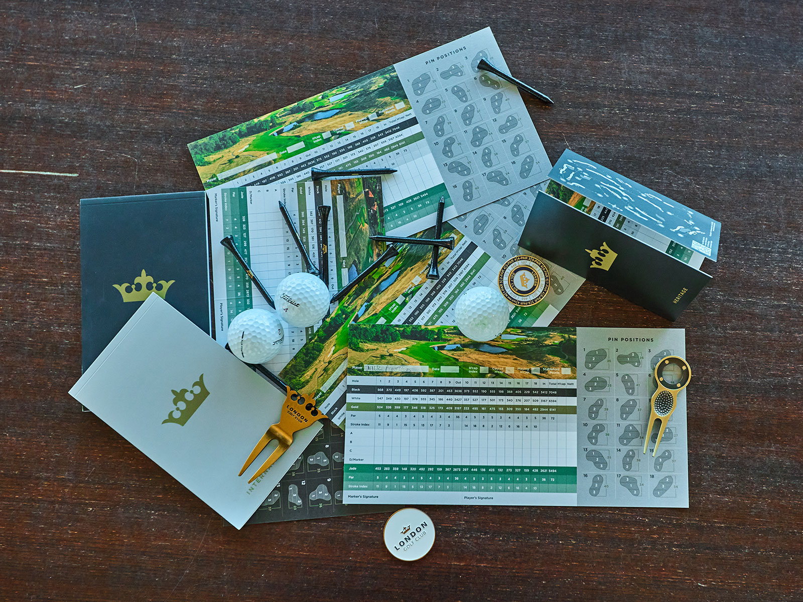 golf scorecards, course planners, balls, ball markers, tees and pitch-mark repairers scattered on a table in a clubhouse