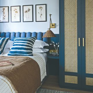 A bedroom with a scalloped blue headboard and a blue wardrobe with cane inserts