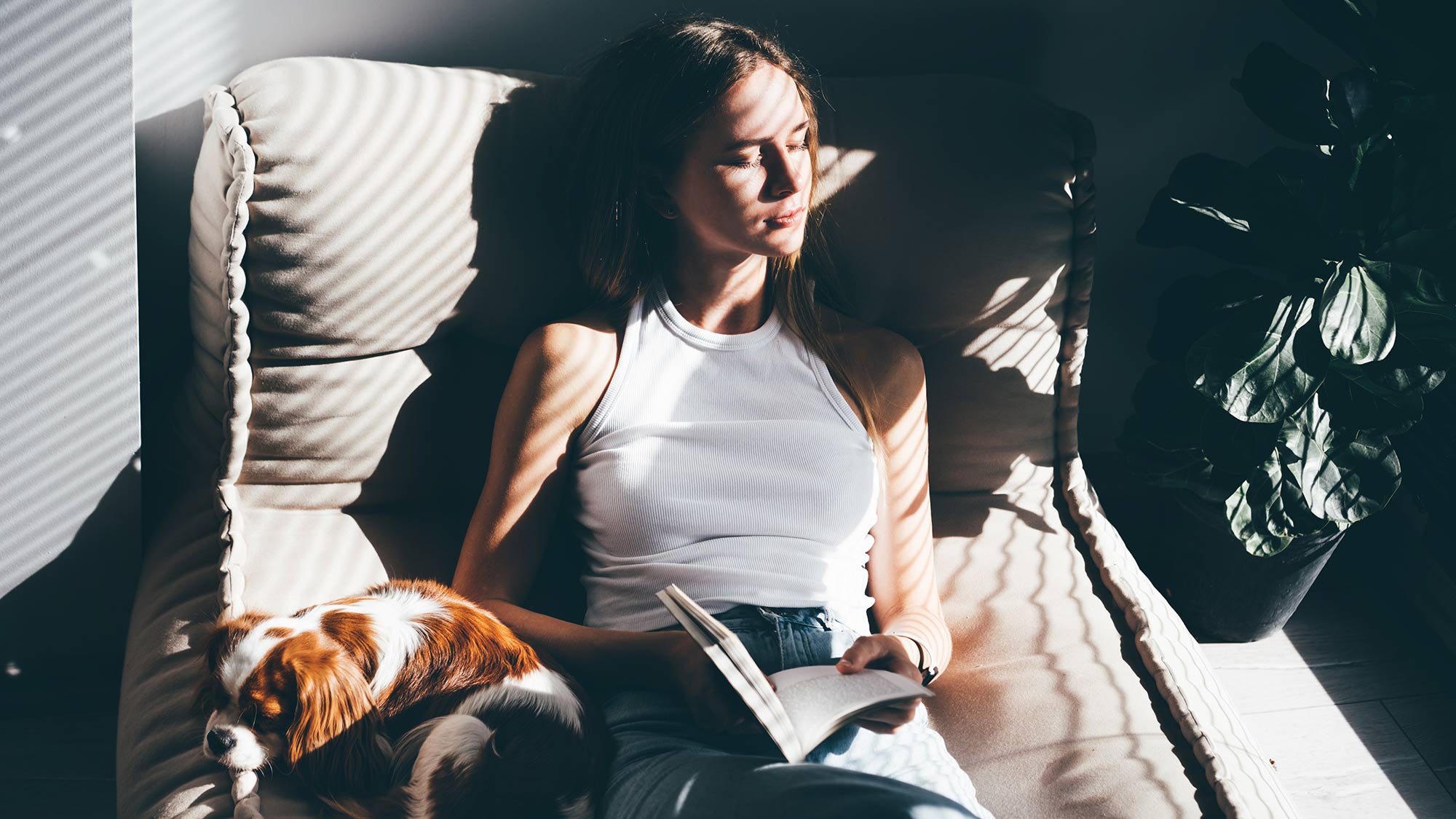 Woman reading a book and cuddling a dog on a sofa.