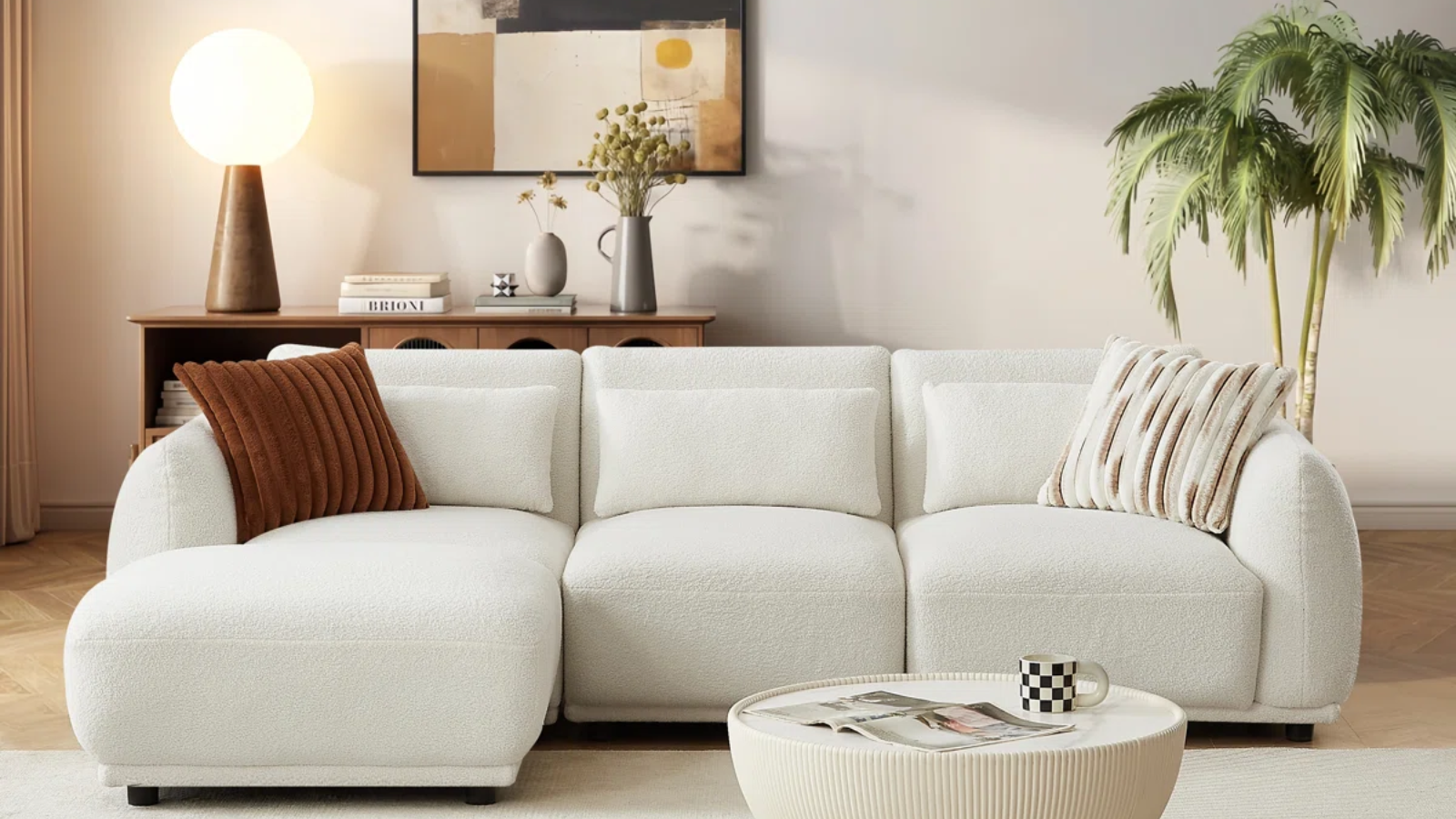 a living room with a white sofa, a round coffee table, and a console table behind holding a lamp and decorative objects