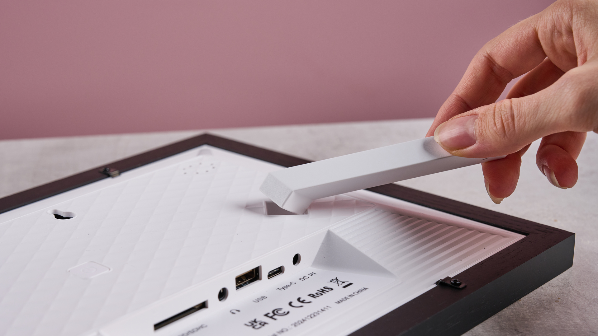 A hand adjusts the stand on the rear of the Eptusmey 10.1-inch WiFi Digital Photo Frame to change its orientation.