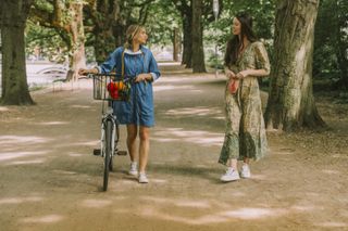Two women with bicycle and face mask walking in park