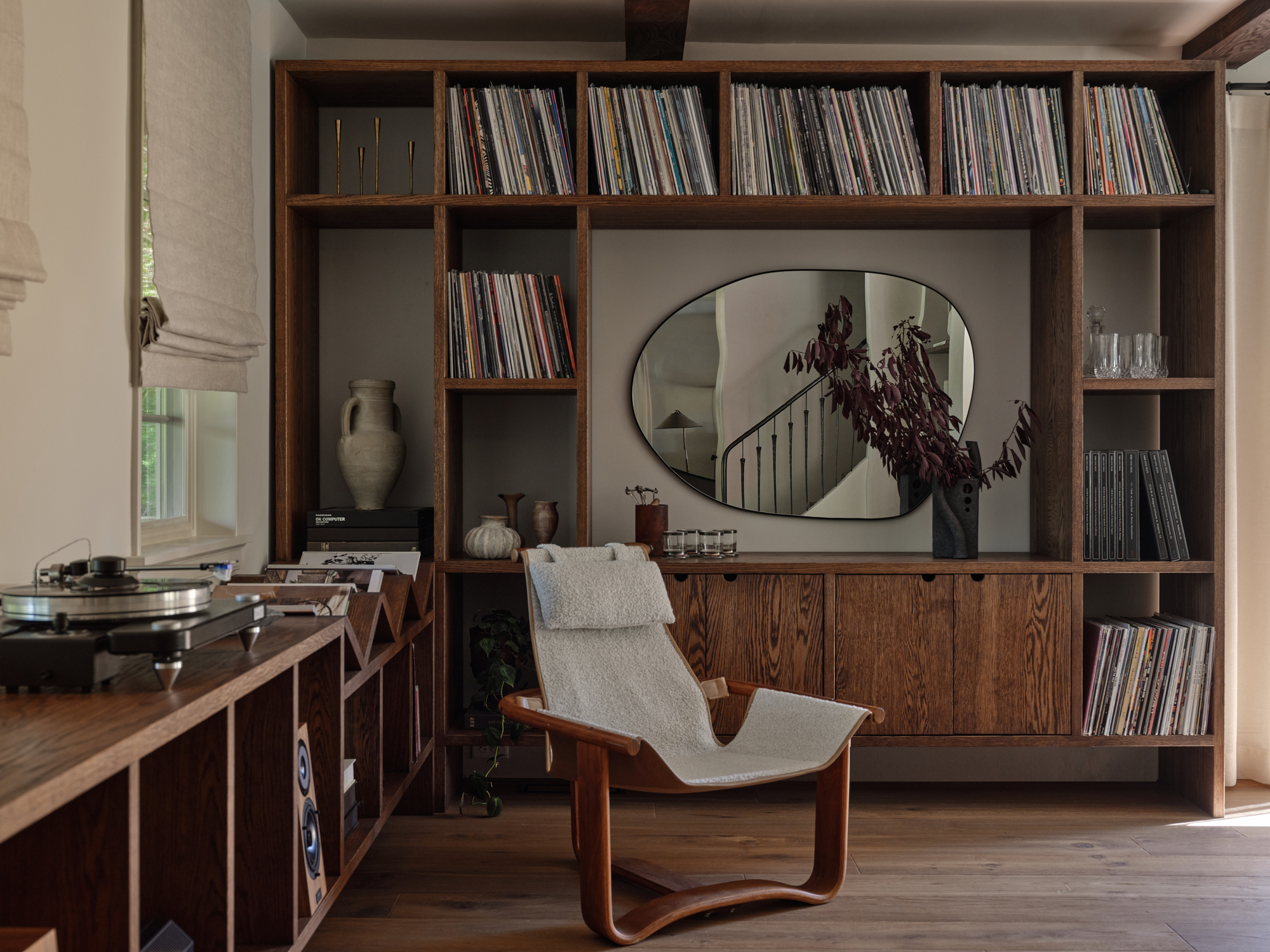 Image of a listening room with custom built-in wooden shelving on the walls and around the room. The shelves are filled with records and there is a record player on the left hand side. In the middle is a white canvas and wood lounge chair.