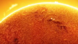 A close up view of the sun showing a swirling orange surface and a bright yellow prominence at the top of the image.