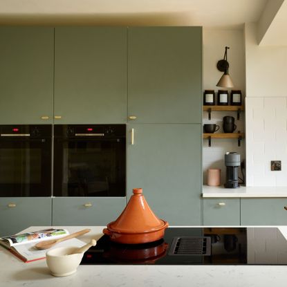 Green/blue cupboards, gold leaf island unit, large patterned tiles above the sink. Wooden dining table, with wooden slatted wall behind