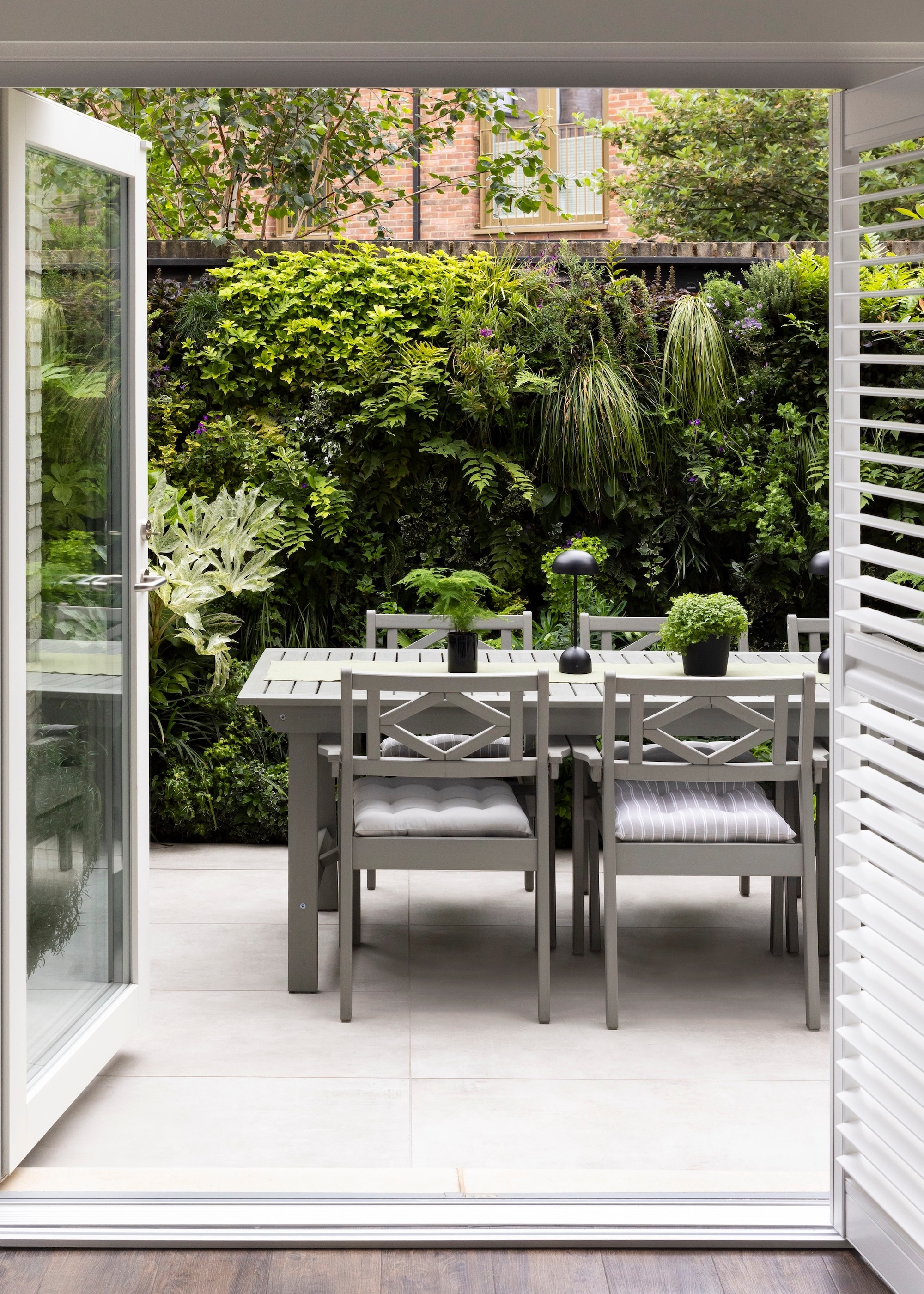 A living wall in an urban garden with tiled patio and grey table and chairs