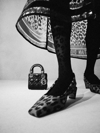View a woman's black and white leopard print shoes and dress with her handbag on the floor behind her.