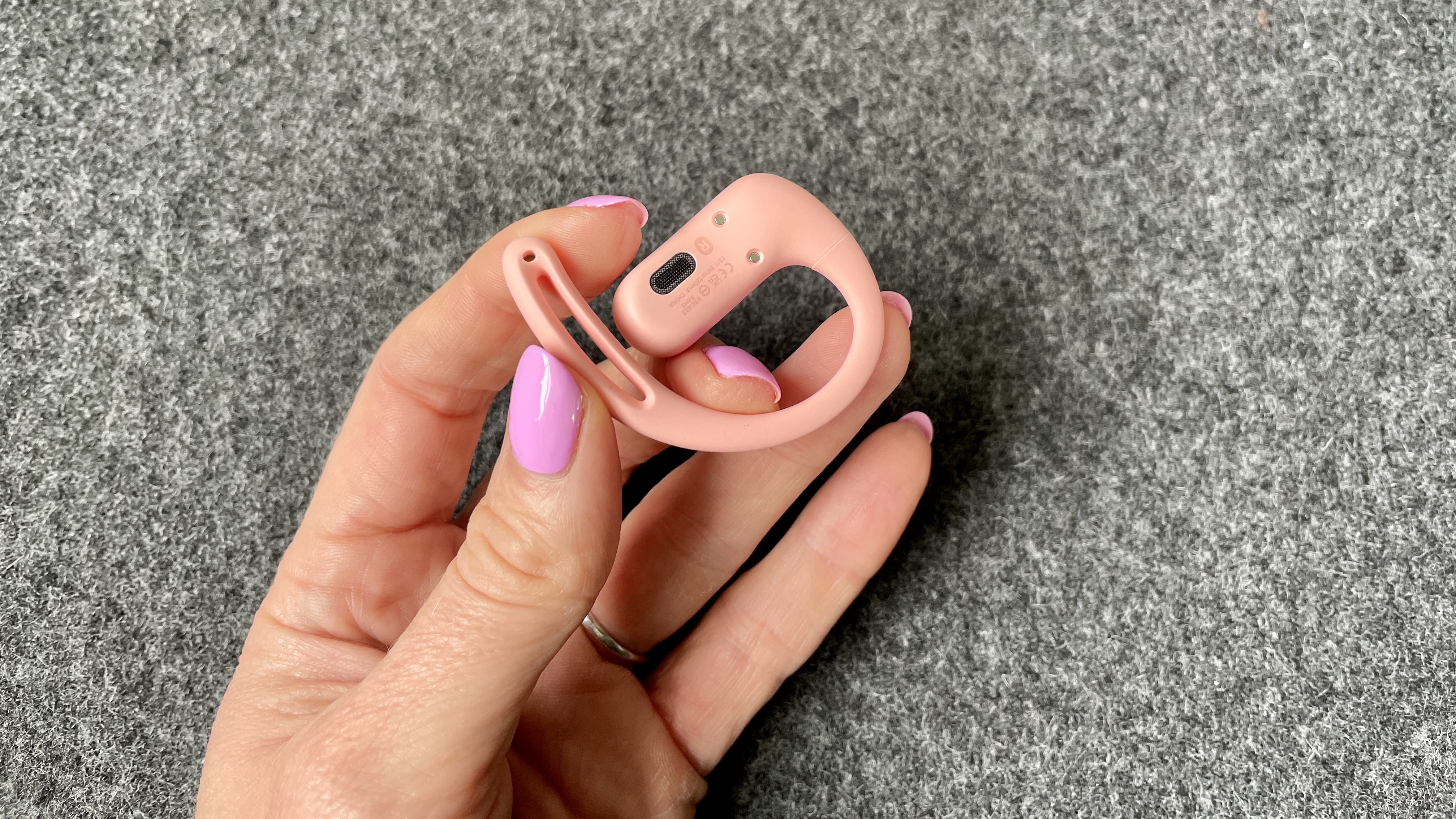 Shokz OpenFit Air in pink, held in a hand wearing pink nail varnish
