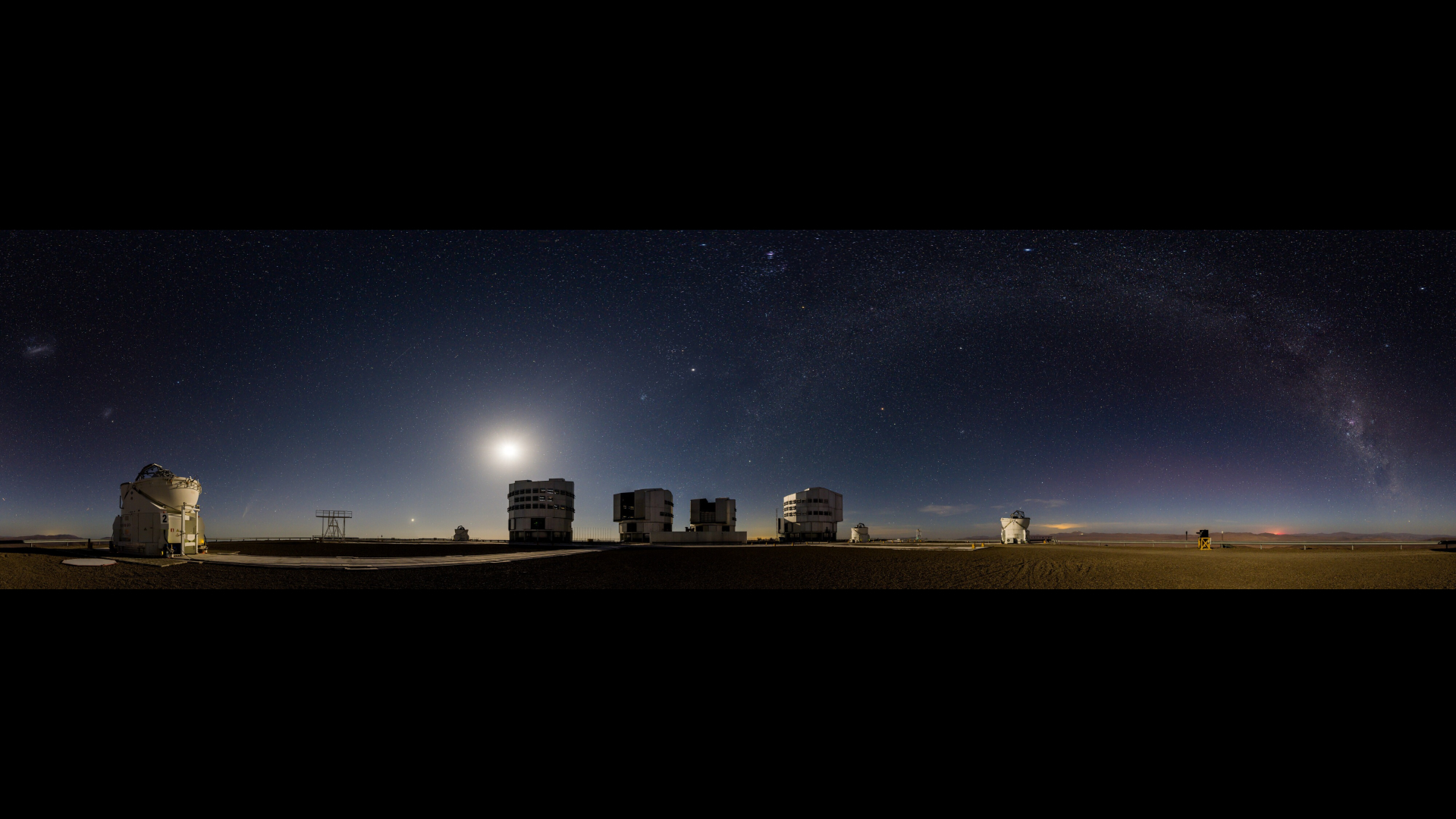 many bright dots can be seen in a starry night sky above a cluster of buildings in a desert